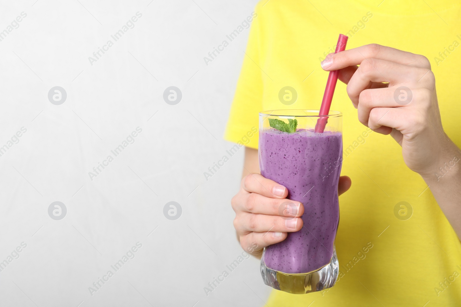 Photo of Woman holding glass of delicious blueberry smoothie on light background, closeup