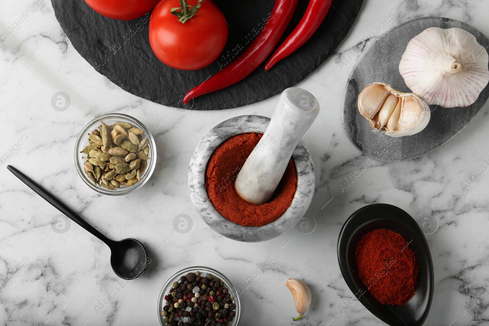 Photo of Mortar with red curry paste and ingredients on white marble table, flat lay