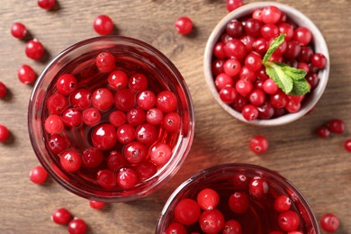 Photo of Tasty cranberry juice in glasses and fresh berries on wooden table, flat lay