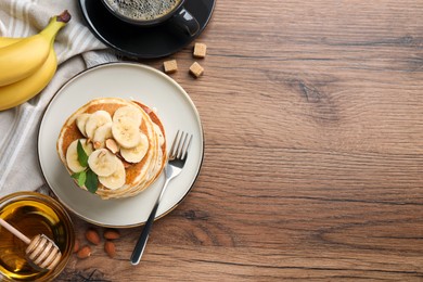 Photo of Tasty pancakes with sliced banana served on wooden table, flat lay. Space for text