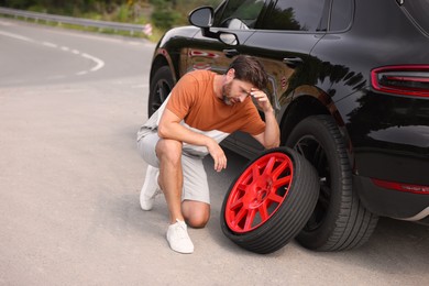 Tire puncture. Stressed man with new wheel near car on roadside outdoors