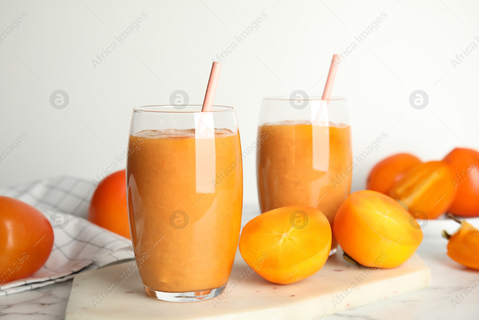 Photo of Tasty persimmon smoothie with straws and fresh fruits on white marble table