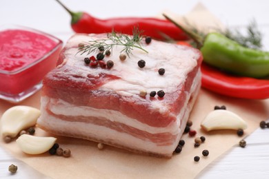 Piece of tasty pork fatback with peppercorns and garlic on white table, closeup