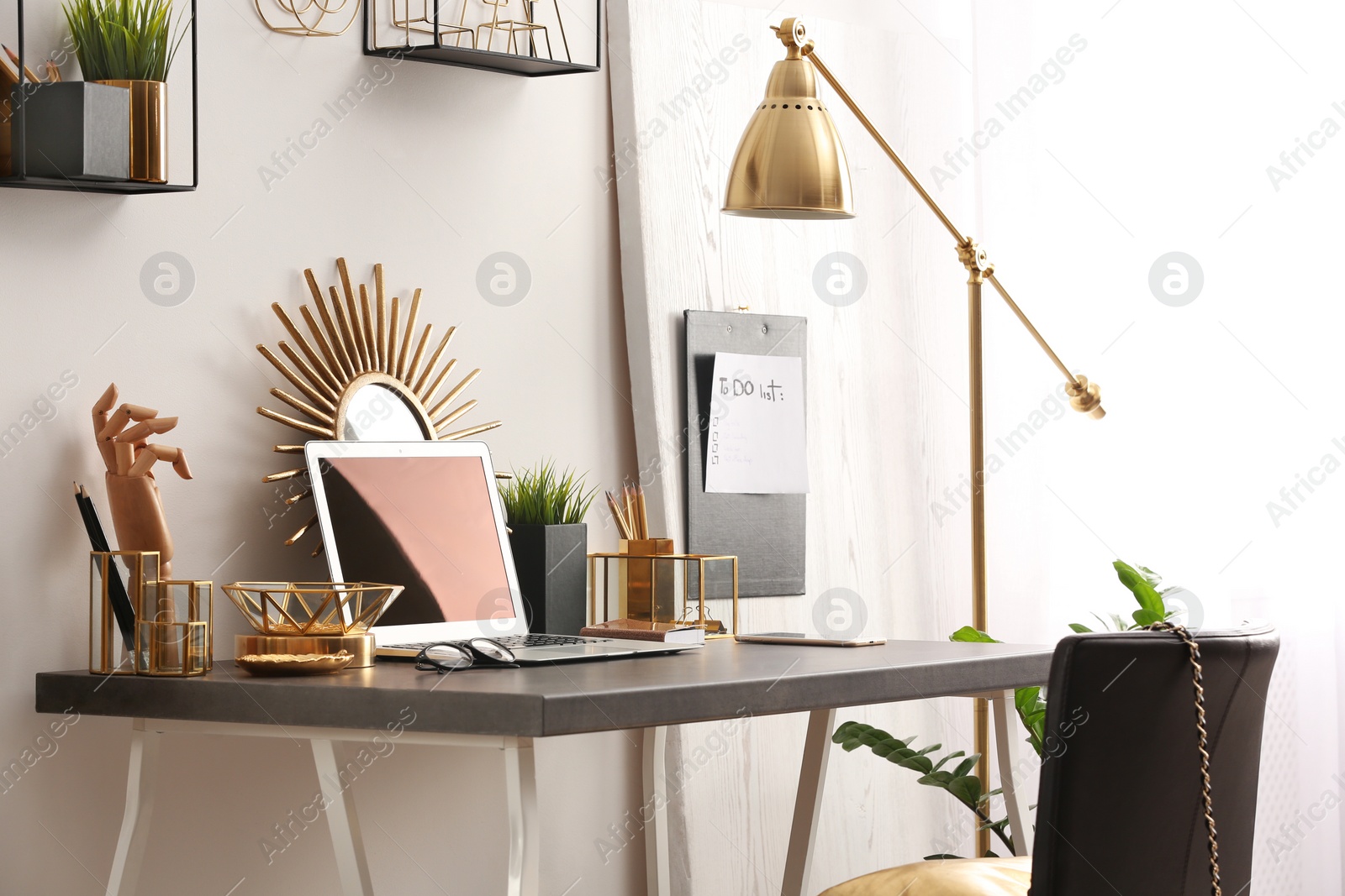 Photo of Modern workplace with laptop and golden decor on desk near wall. Stylish interior design