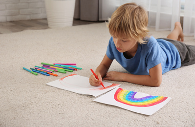 Photo of Little boy drawing rainbow on floor indoors. Stay at home concept