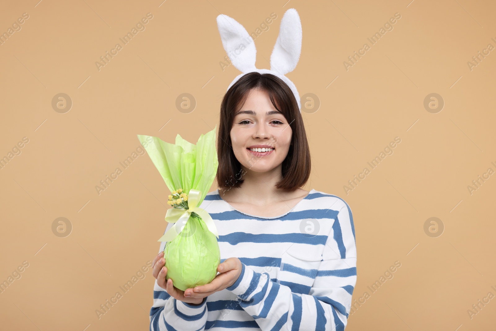 Photo of Easter celebration. Happy woman with bunny ears and wrapped egg on beige background