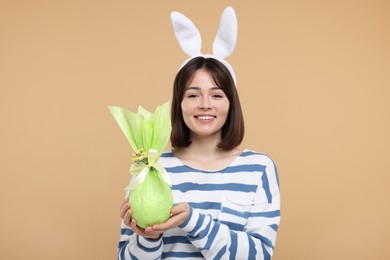 Easter celebration. Happy woman with bunny ears and wrapped egg on beige background