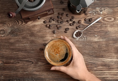 Woman with glass of aromatic hot coffee at wooden table, top view