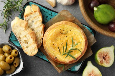 Photo of Tasty baked brie cheese and products on grey table, flat lay