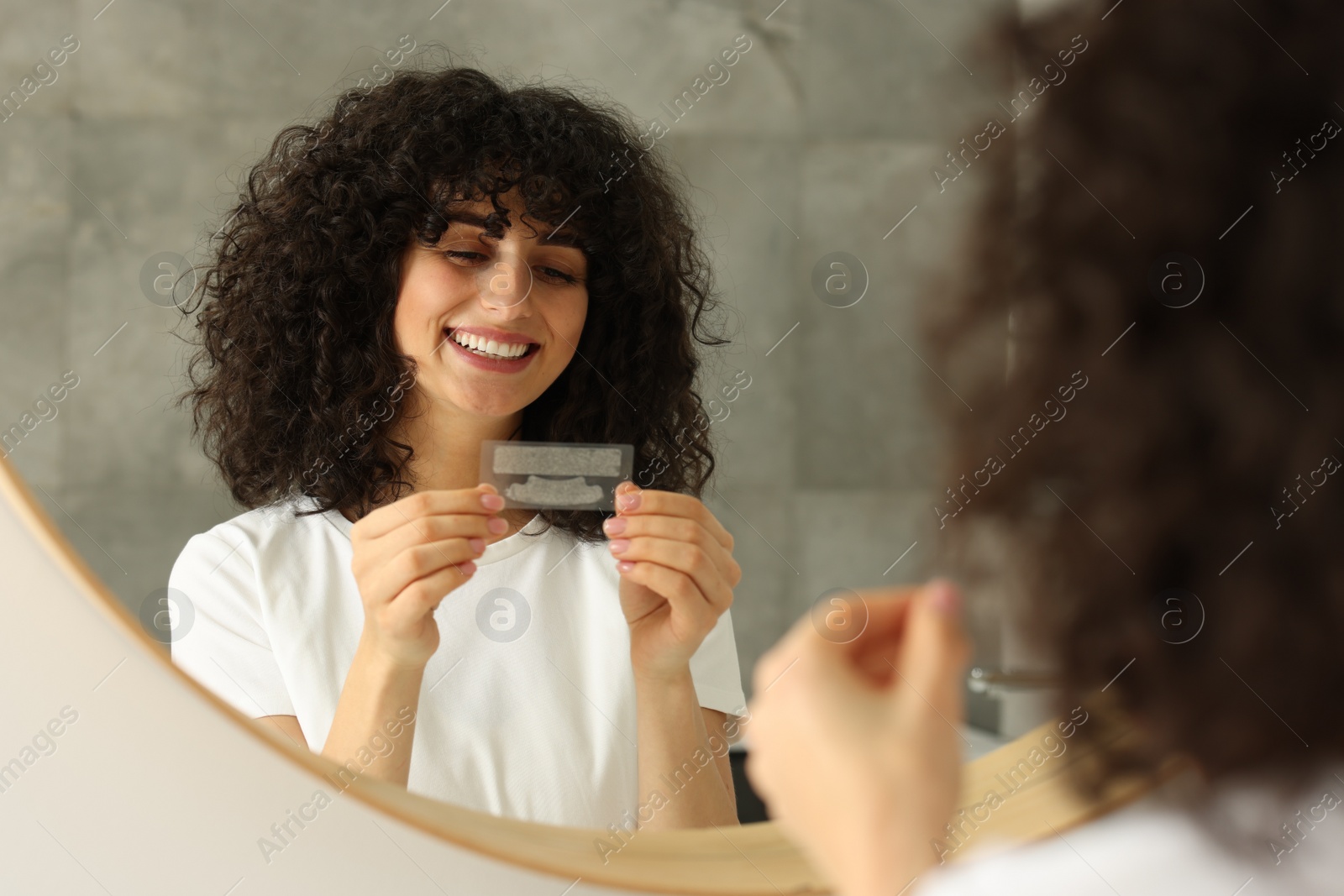 Photo of Young woman holding teeth whitening strips indoors