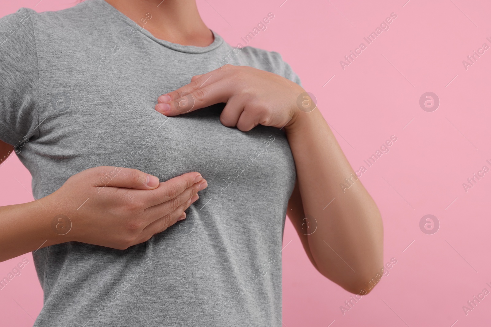 Photo of Woman doing breast self-examination on pink background, closeup