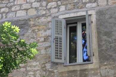 Open window with wooden shutters on wall of old residential building