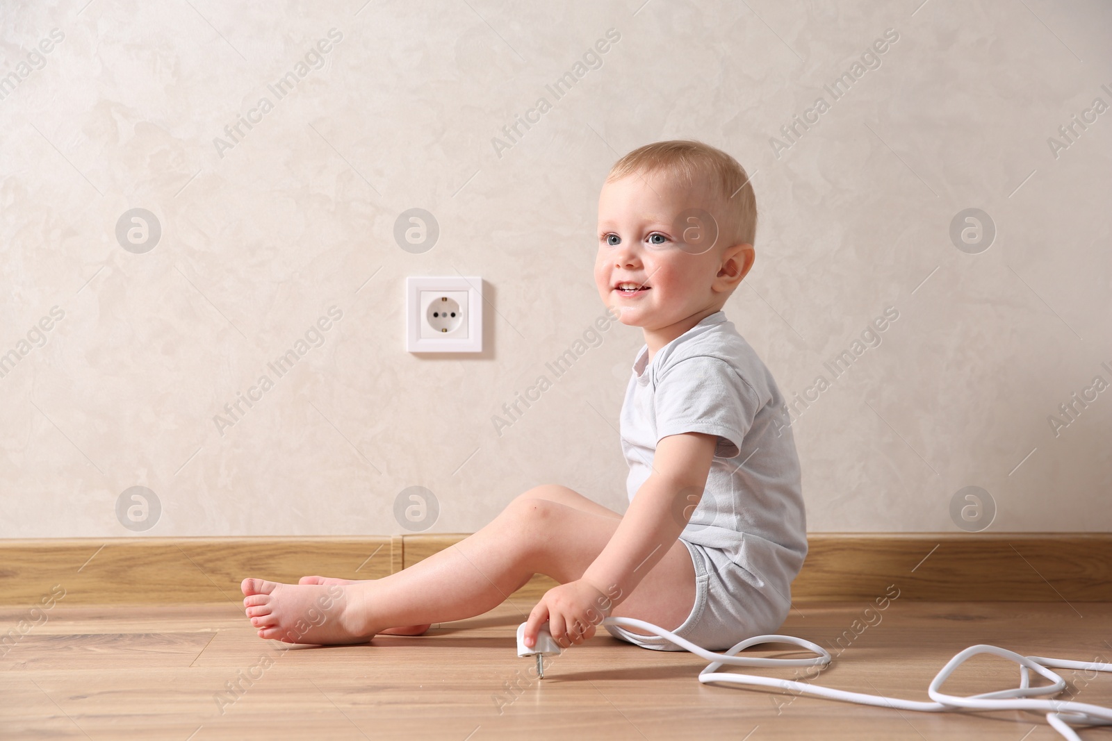 Photo of Little child playing with plug near electrical socket indoors. Dangerous situation