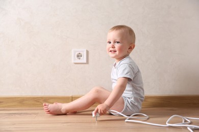 Photo of Little child playing with plug near electrical socket indoors. Dangerous situation