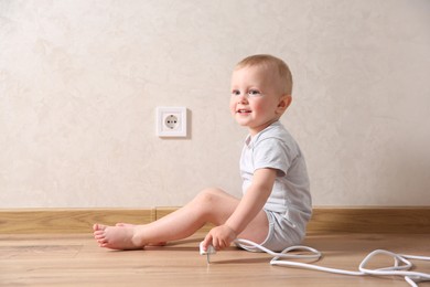 Little child playing with plug near electrical socket indoors. Dangerous situation