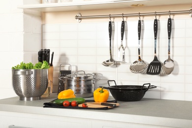 Photo of Set of clean cookware, utensils and products on table in modern kitchen