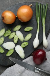 Board with different kinds of onions and knife on grey table, flat lay