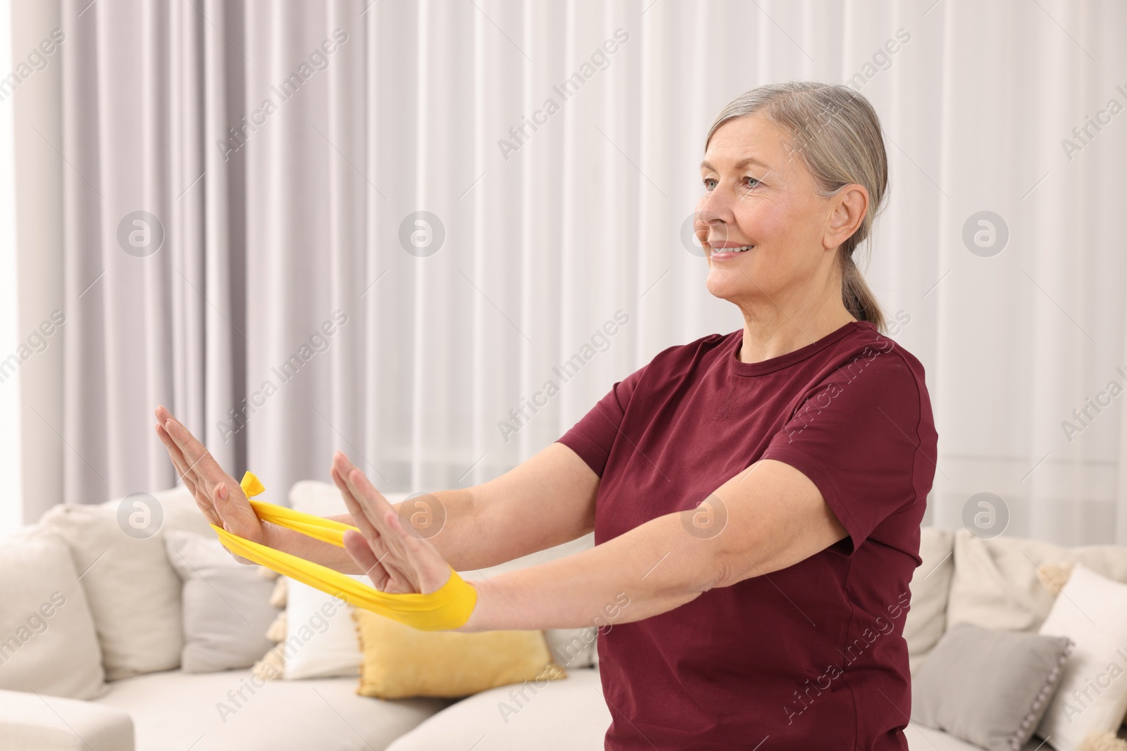 Photo of Senior woman doing exercise with fitness elastic band at home