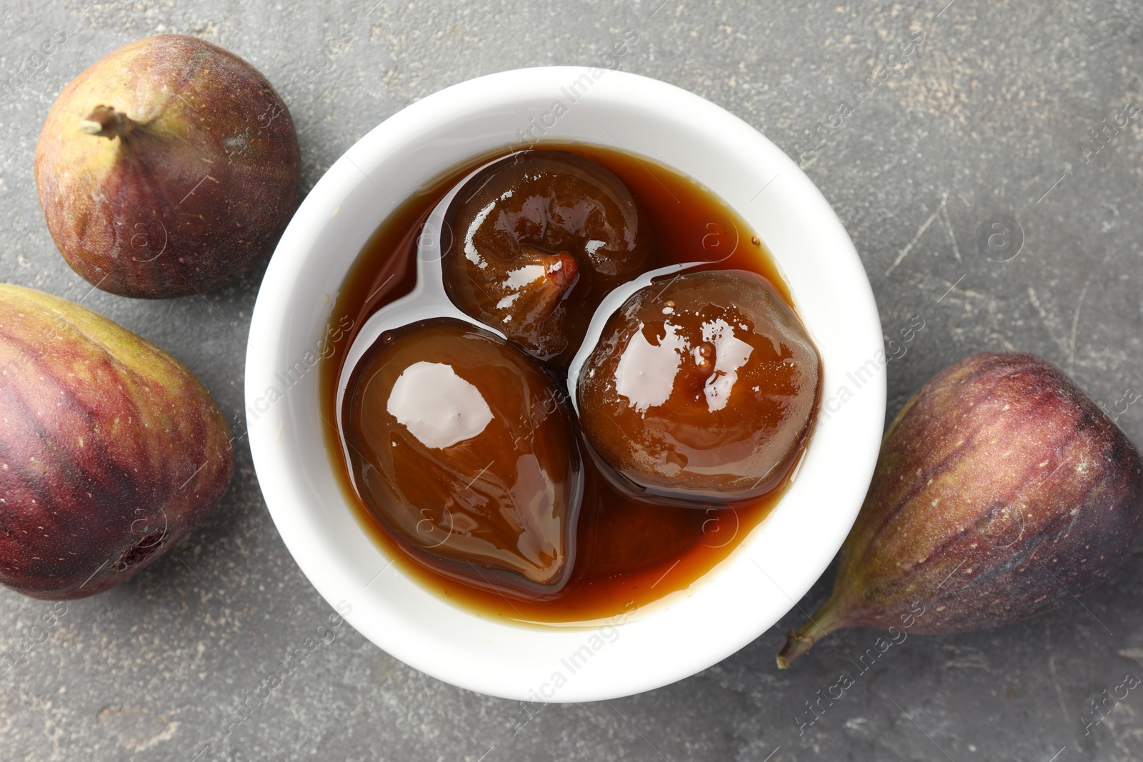 Photo of Bowl of tasty sweet jam and fresh figs on grey table