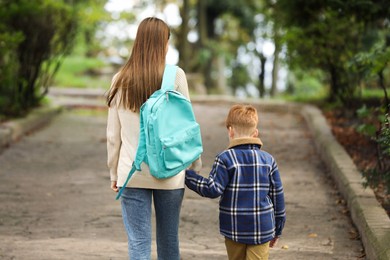Photo of Young mom taking her son to school, back view