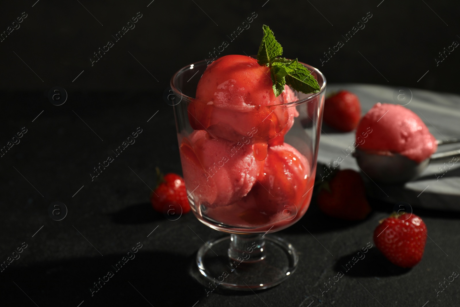 Photo of Delicious strawberry ice cream in dessert bowl on black table against dark background