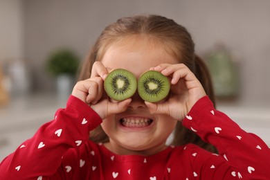 Photo of Funny girl covering eyes with halves of fresh kiwi indoors