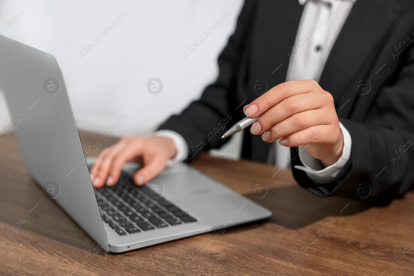 Photo of Woman with pen working on laptop at wooden table, closeup. Electronic document management