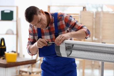 Photo of Professional technician repairing electric infrared heater with screwdriver indoors