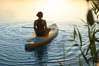 Woman paddle boarding on SUP board in river at sunset, back view