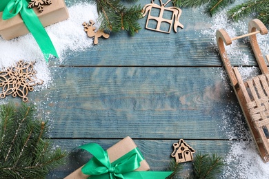 Flat lay composition with sleigh, fir tree branches and gift boxes on blue wooden table, space for text