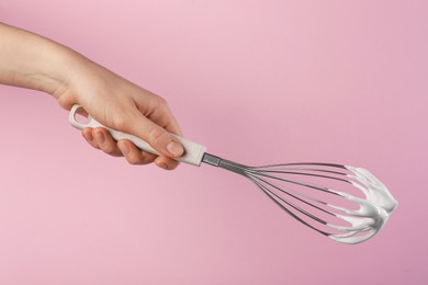 Photo of Woman holding whisk with whipped cream on pink background, closeup