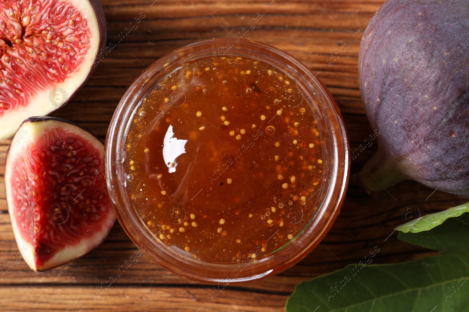 Photo of Jar of tasty sweet jam and fresh figs on wooden table, flat lay