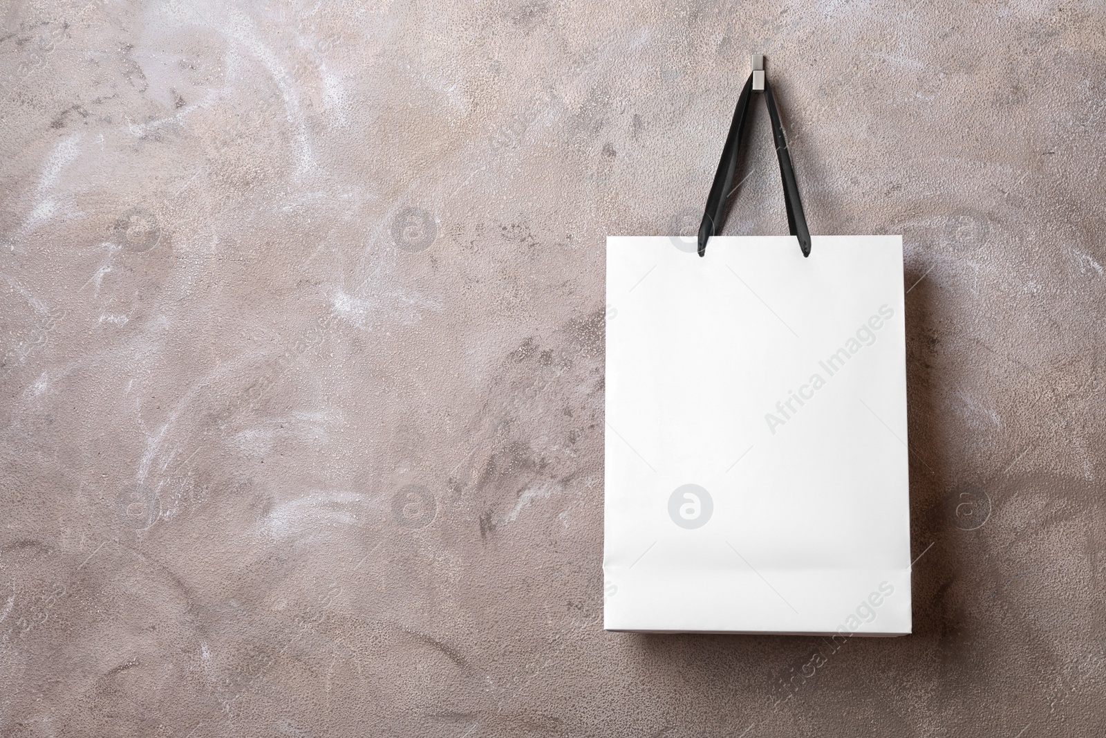 Photo of Paper shopping bag with handles hanging on color wall. Mock up for design