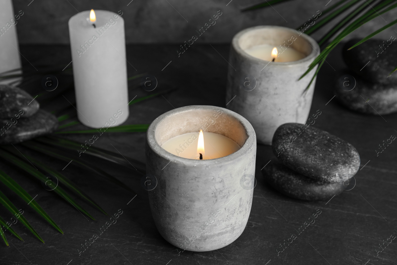 Photo of Burning candles, spa stones and palm leaf on dark grey table