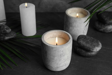 Photo of Burning candles, spa stones and palm leaf on dark grey table