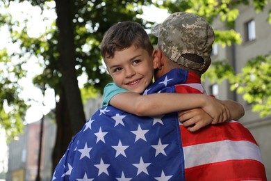 Photo of Soldier with flag of USA and his little son hugging outdoors