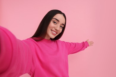 Photo of Smiling young woman taking selfie on pink background, space for text