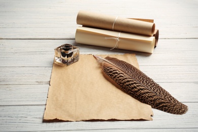 Photo of Feather pen, inkwell and blank parchment on wooden table