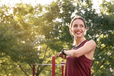 Young woman with wireless headphones listening to music while exercising on sports ground. Space for text