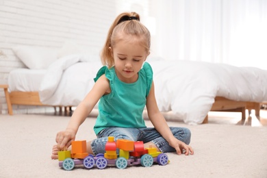 Photo of Cute child playing with wooden train on floor at home