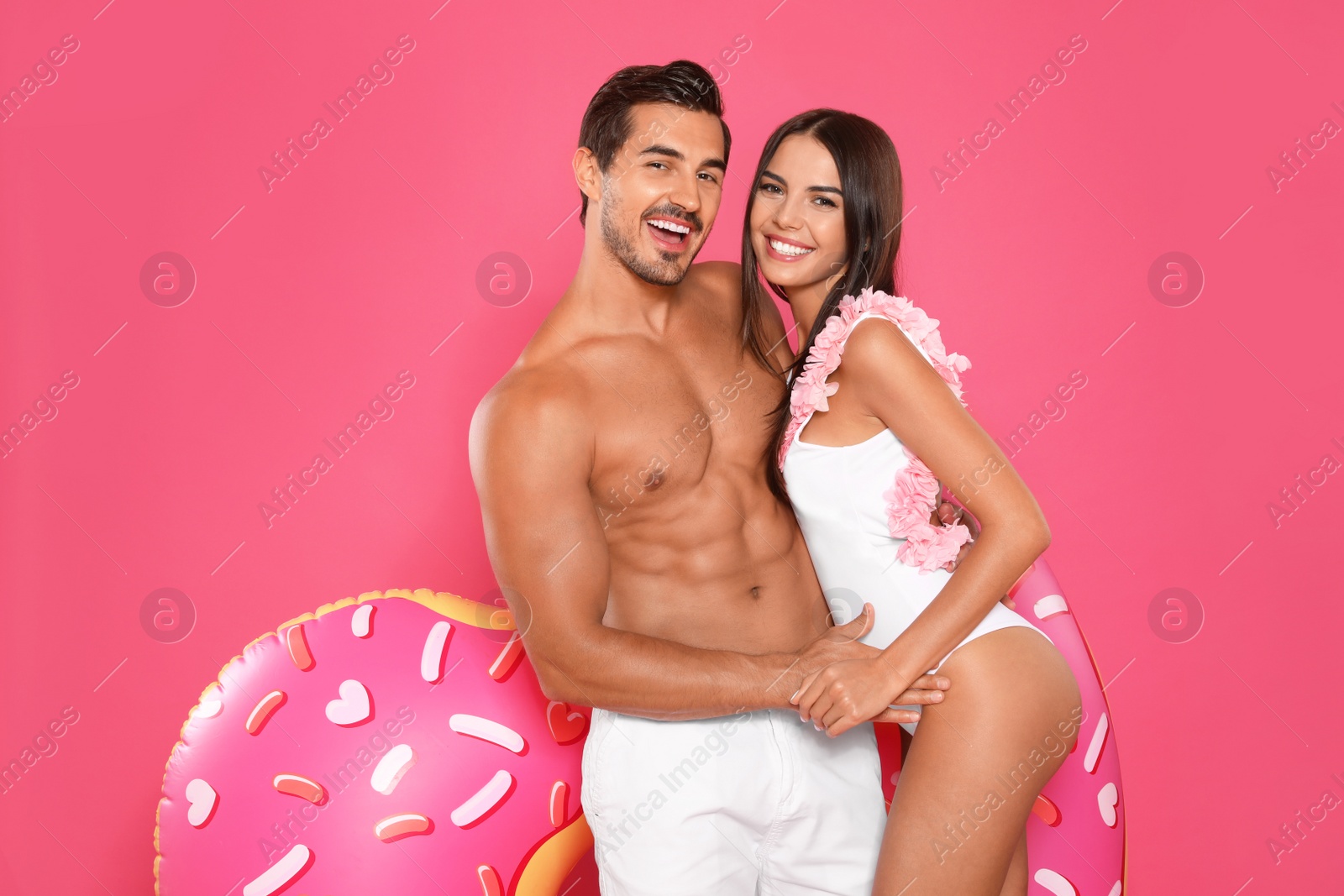 Photo of Young attractive couple in beachwear with inflatable ring on pink background