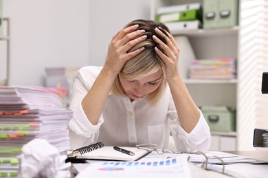 Overwhelmed woman at table with many documents in office