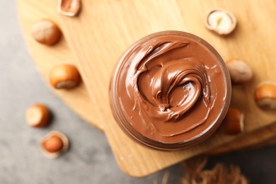 Photo of Tasty chocolate hazelnut spread and nuts on wooden board, flat lay. Space for text