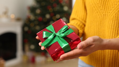 Photo of Woman with beautifully wrapped Christmas gift indoors, closeup