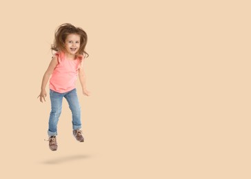 Cute girl jumping on beige background, space for text