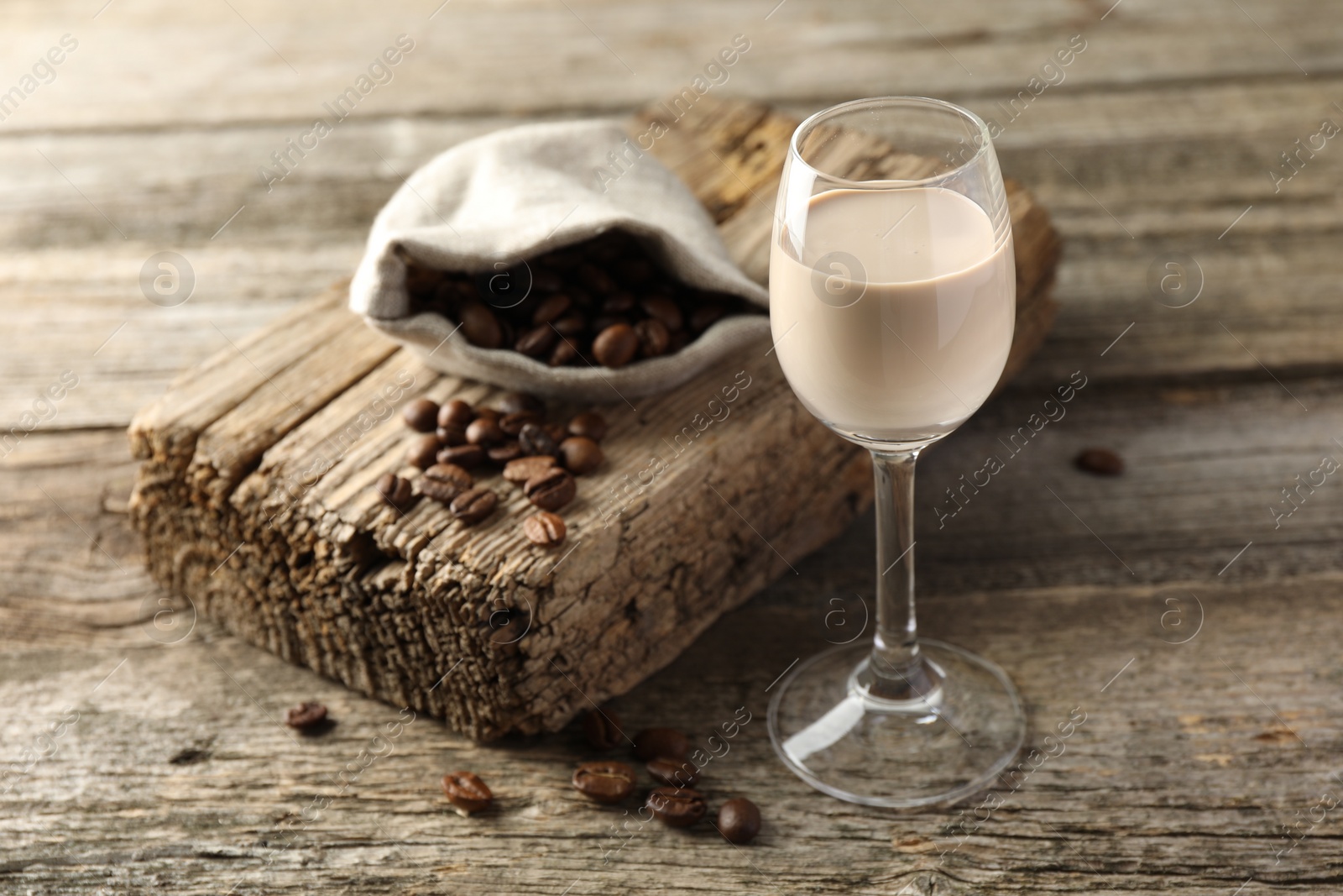 Photo of Coffee cream liqueur in glass and beans on wooden table