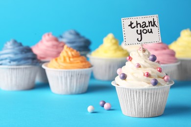 Photo of Tasty cupcakes and note with phrase Thank You on light blue background, space for text