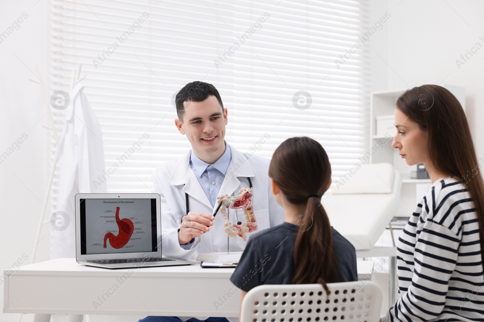 Photo of Gastroenterologist with model of intestine consulting woman and her daughter in clinic