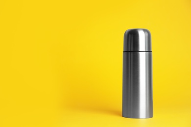 Stylish thermo bottle on yellow background, space for text