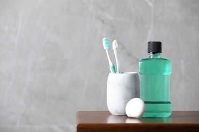Photo of Bottle of mouthwash, toothbrushes and dental floss on wooden table, space for text